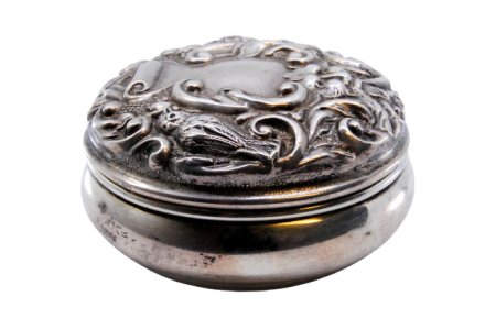 Caixa de comprimidos em prata com interior dourado e relevada na tampa amovível.